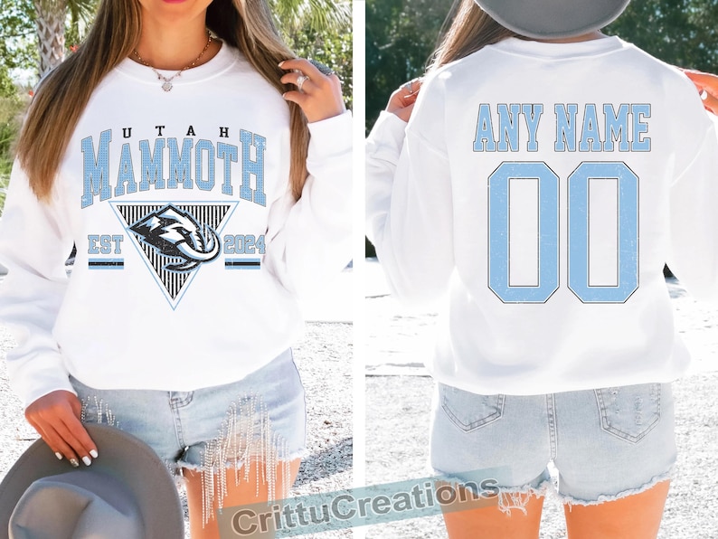 Puede incluir: Sudadera blanca con "UTAH MAMMOTH" en letras de bloque azul claro. La parte delantera presenta un logotipo del equipo y "EST 2024". La parte trasera muestra "ANY NAME" y el n&uacute;mero "00" en azul claro. Una prenda deportiva informal.