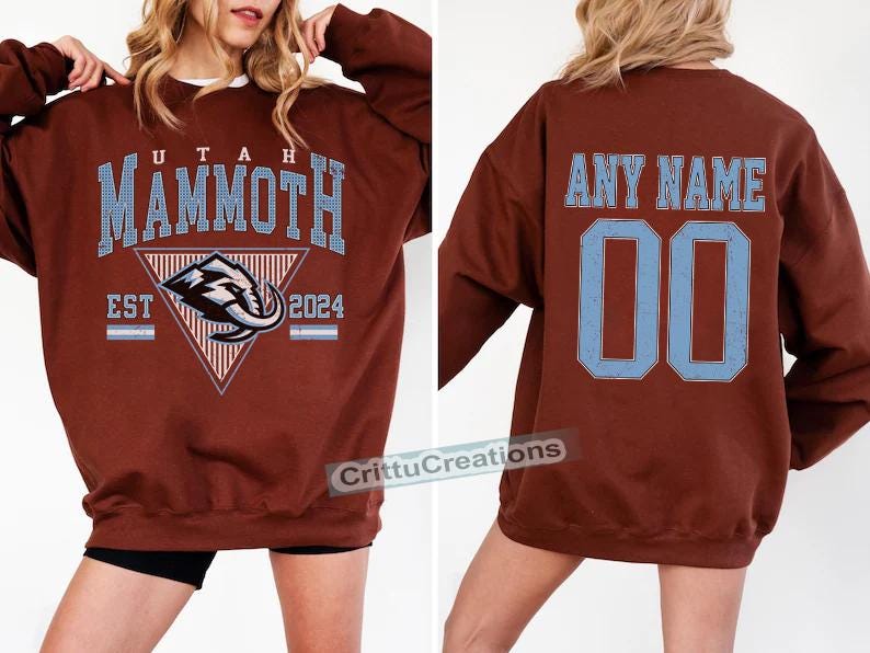 Puede incluir: Sudadera granate con el texto "UTAH MAMMOTH" en azul claro, un logotipo de mamut y "EST 2024". La parte trasera muestra "ANY NAME" y el n&uacute;mero "00" en azul claro. La sudadera tiene cuello redondo y es una prenda informal.
