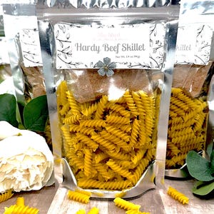 Può includere: Un sacchetto richiudibile argentato pieno di pasta gialla e un piccolo pacchetto di condimento. Il sacchetto ha un'etichetta con la scritta "Hardy Beef Skillet" con un design floreale. Peso netto: 94 g (3,4 oz).