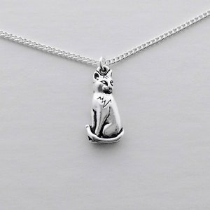 May include: A silver chain necklace with a small, silver cat pendant. The cat is sitting with its tail curled around its legs.