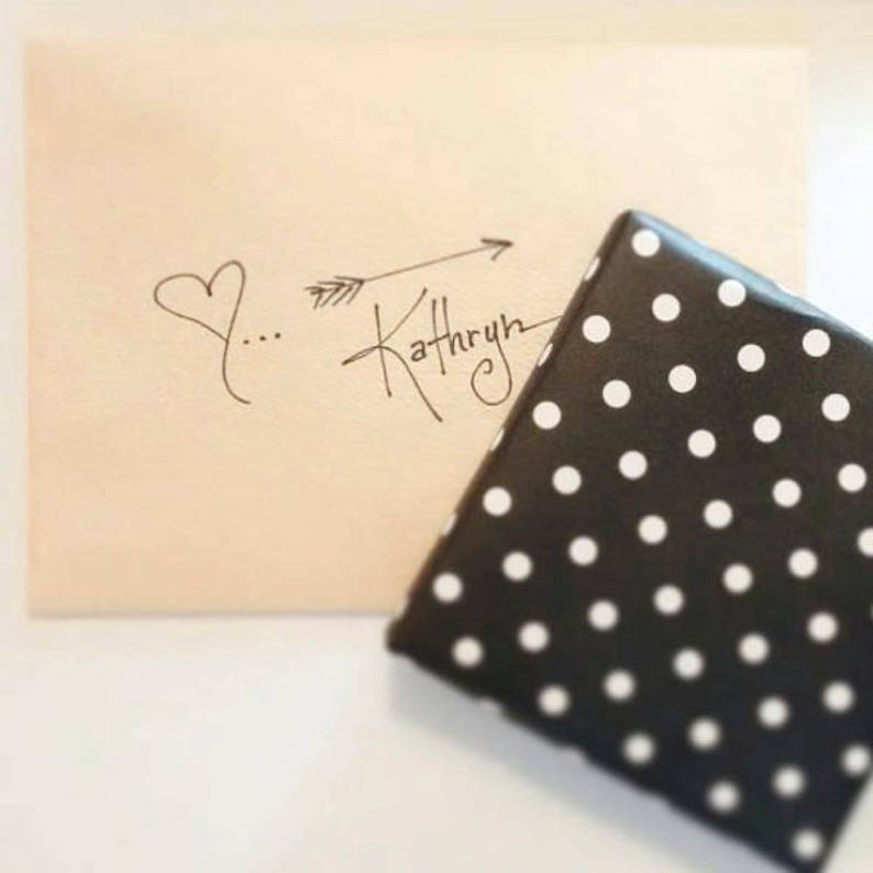 May include: A white heart with three dots and an arrow pointing to the right with the word "Kathryn" written in cursive.