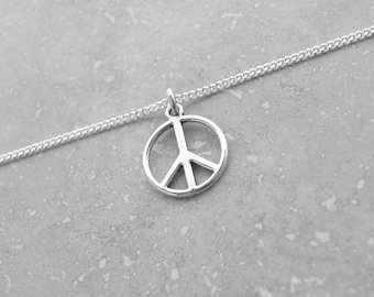 May include: A silver peace sign pendant necklace on a silver chain. The necklace is on a gray background.
