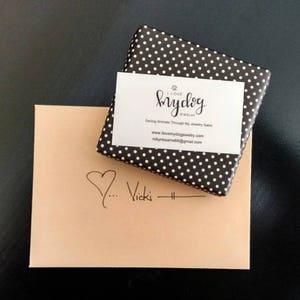 May include: A brown envelope with a handwritten heart and the name "Vicki" on it. A small black and white polka dot box with a white business card that reads "I Love My Dog Jewelry" and "Saving Animals Through My Jewelry Sales" is on top of the envelope.