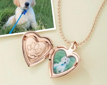 May include: A rose gold heart-shaped locket necklace with a small photo of a golden retriever puppy inside. The locket is open, revealing a paw print design on the inside. The necklace chain is a delicate ball chain.