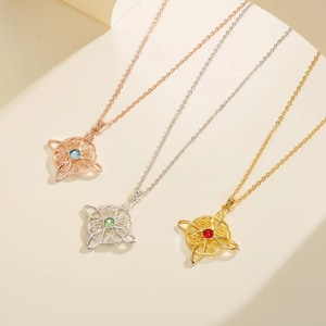 May include: Three necklaces with Celtic knot pendants. One is rose gold with a blue gem, one is silver with a green gem, and one is gold with a red gem. The pendants have an openwork design and are suspended from delicate chains.