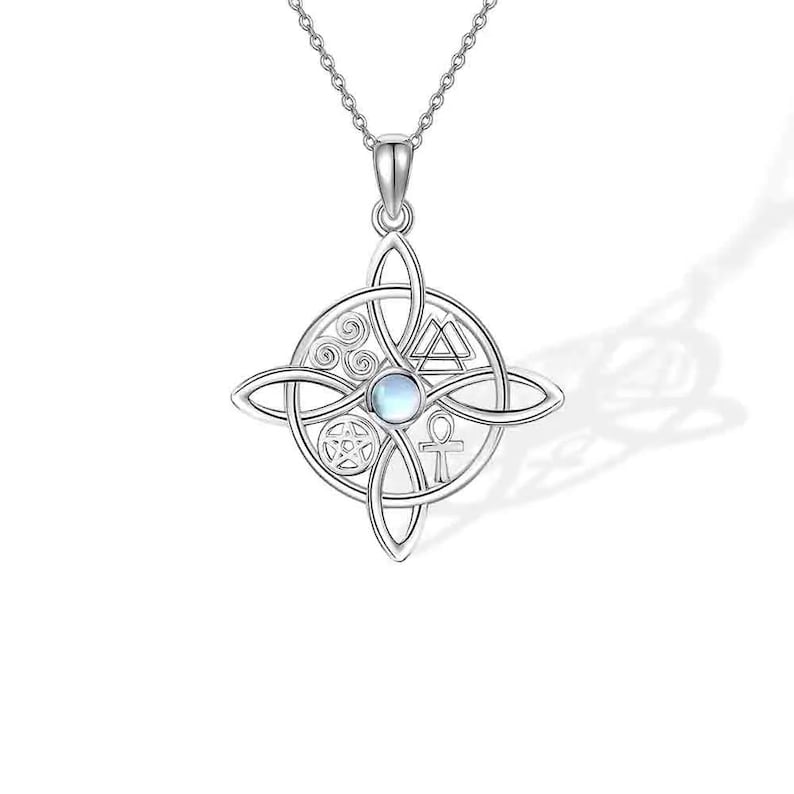 May include: A silver-colored pendant necklace featuring a Celtic knot design with a central circular element. The circle contains various symbols, including a pentagram, ankh, and triangle. The pendant has a small, round, light-colored stone in the center.