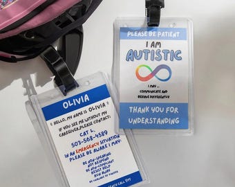 Puede incluir: Dos tarjetas de identificación de plástico transparente con correas negras. Una tarjeta dice "OLIVIA" y proporciona información de contacto e instrucciones de emergencia. La otra tarjeta dice "SOY AUTISTA" con un símbolo de infinito arcoíris y un mensaje sobre la comunicación.