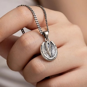 May include: Silver-toned horseshoe pendant necklace. The pendant features a detailed horseshoe design with a central element. The necklace has a chain with a textured, woven appearance. The jewelry is held in a hand.