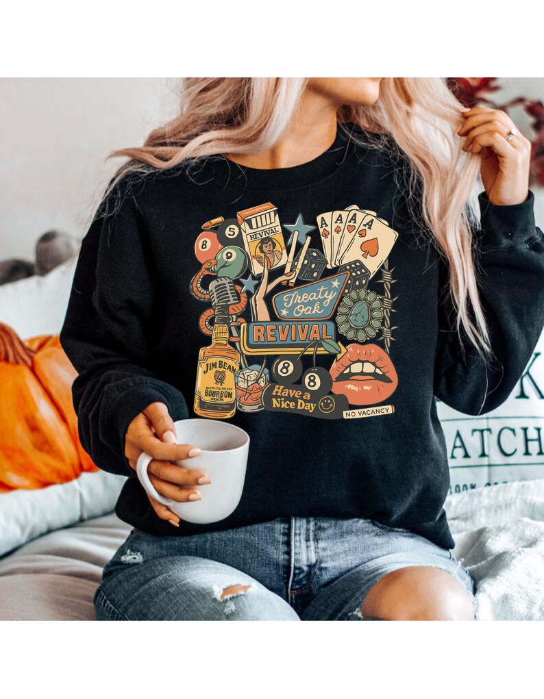 Peut inclure: Sweat-shirt noir &agrave; col rond avec un motif r&eacute;tro. Le motif comprend une bouteille de bourbon Jim Beam, des cartes &agrave; jouer, un microphone et les mots "Treaty Oak Revival" et "Have a Nice Day".