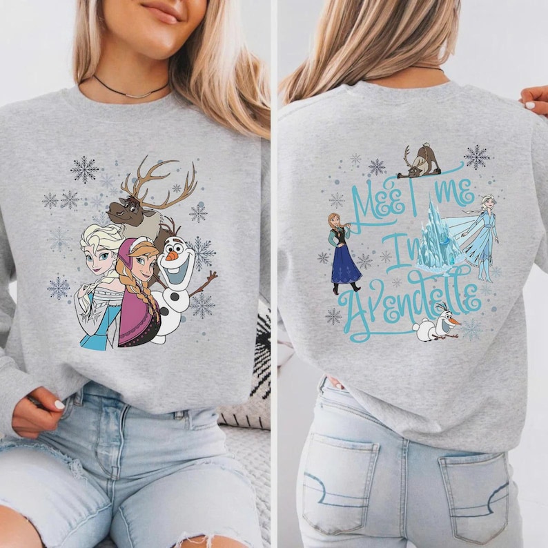 Peut inclure: Un sweat-shirt gris avec des personnages du film d'animation "La Reine des Neiges". Le devant montre Elsa, Anna, Olaf et Sven, avec des flocons de neige. Le dos porte l'inscription "Meet me in Arendelle" avec d'autres personnages et flocons.