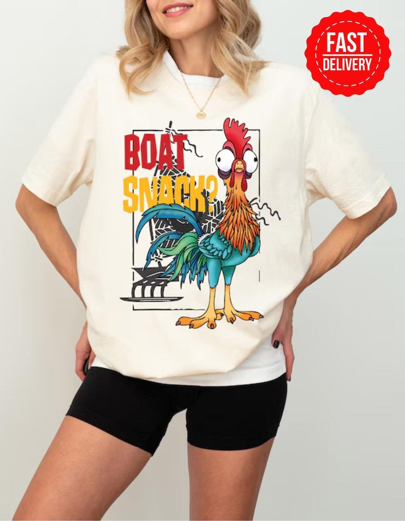 Puede incluir: Camiseta color crema con un gallo de dibujos animados y el texto "BOAT SNACKS?" en rojo y amarillo. El gallo tiene una cresta roja, plumas naranjas y azules y ojos grandes. Una pegatina roja de "FAST DELIVERY" es visible.
