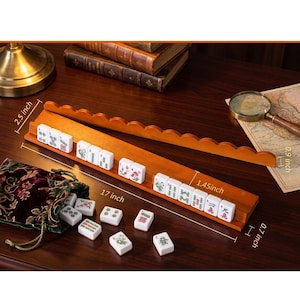 May include: A wooden Mahjong set with white tiles featuring floral and character designs. The set includes a 17-inch long wooden rack and a velvet bag. The rack is 2.5 inches wide and 0.7 inches high.