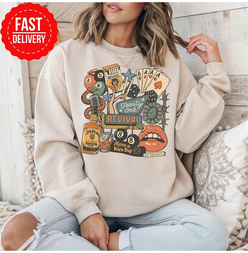 Peut inclure: Sweat-shirt beige avec un motif color&eacute; repr&eacute;sentant une bouteille de bourbon Jim Beam, des cartes &agrave; jouer, des d&eacute;s et les mots "Treaty Oak Revival" et "Have a Nice Day". Le motif comprend des l&egrave;vres et un panneau "No Vacancy".