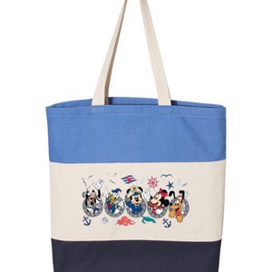 May include: A blue, white, and navy blue striped canvas tote bag with a design of Mickey Mouse, Minnie Mouse, Goofy, Donald Duck, and Pluto in a nautical theme. The characters are wearing sailor hats and are peeking out of portholes.