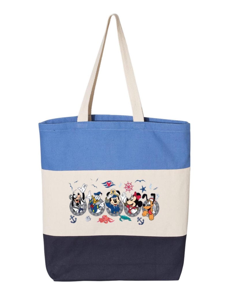 May include: A blue, white, and navy blue striped canvas tote bag with a design of Mickey Mouse, Minnie Mouse, Goofy, Donald Duck, and Pluto in a nautical theme. The characters are wearing sailor hats and are peeking out of portholes.