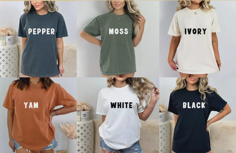 May include: Six short-sleeved t-shirts in various colors: pepper, moss, ivory, yam, white, and black. Each shirt has a different color name printed in bold, white capital letters across the chest. The shirts are worn by different people.