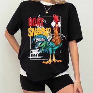 Puede incluir: Camiseta negra con un dise&ntilde;o de gallo de dibujos animados y el texto "BOAT SNACKS?". El gallo tiene plumas rojas, naranjas, azules y verdes. La camiseta tiene cuello blanco y se combina con pantalones cortos negros.