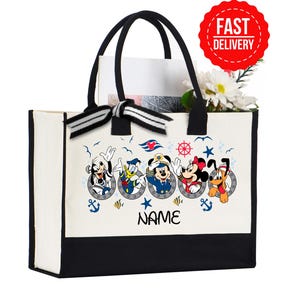 May include: A white and black tote bag featuring Disney characters in sailor outfits. The bag has black handles and a black bottom. The text "NAME" is below the characters. A red "FAST DELIVERY" sticker is visible.