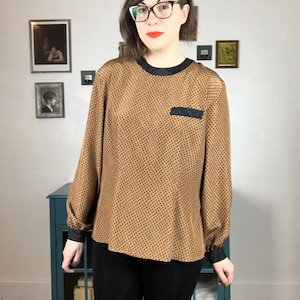 May include: A brown and black polka dot blouse with a black collar and a black pocket on the left side. The blouse has long sleeves with black cuffs.