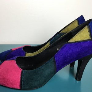 May include: A pair of colorful suede pumps. The shoes feature a patchwork design with panels of blue, pink, green, and olive green. The heels are black and the shoes have a pointed toe.