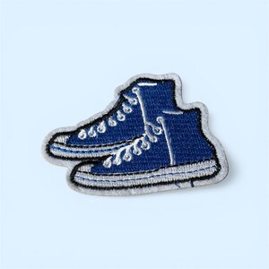 May include: Embroidered patch featuring a pair of blue high-top sneakers with white laces and stitching. The patch has a white border and is set against a light blue background.