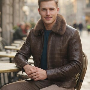May include: A brown jacket with a textured crocodile-skin pattern and a thick, plush brown fur collar. The jacket features a front zipper closure and is worn over a dark teal shirt, paired with light brown trousers.