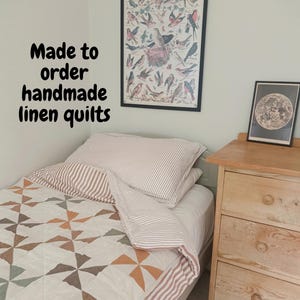 May include: A bed featuring a quilt with a geometric pinwheel pattern in muted tones of rust, sage green, and cream, paired with a striped pillowcase. The text "Made to order handmade linen quilts" is visible on the wall above the bed.