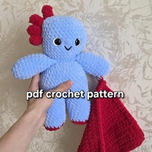 May include: A light blue plush toy with a red crest and red feet, featuring black and white eyes and a stitched smile. A separate red textured fabric piece is attached to the toy. The text "pdf crochet pattern" is overlaid on the image.