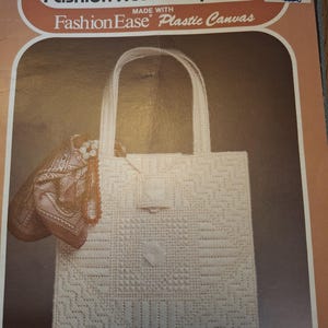 May include: A craft instruction booklet titled Columbia Minerva Fashion Accessory Ideas Made With FashionEase Plastic Canvas featuring a white plastic canvas tote bag with a geometric pattern, a brown patterned scarf, and a beaded necklace.