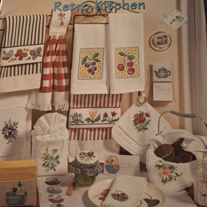 May include: A Jeanette Crews Designs craft pattern book titled TGIF! Retro Kitchen featuring 18 weekend projects. The cover displays various white kitchen textiles including towels, a tissue cover, and a basket liner, all decorated with colorful cross-stitch embroidery of flowers, fruits, and butterflies.