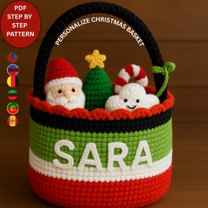 May include: A crochet Christmas basket with a black handle and rim, featuring a red, green, and white striped design. The basket is personalised with the name "SARA" and filled with crochet Christmas figures, including Santa, a tree, and a cloud.
