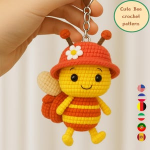 May include: A crocheted bee keychain with a red hat and striped body. The bee has a smiling face, black eyes, and a small white flower on its hat. The keychain includes the text "Cute Bee crochet pattern".