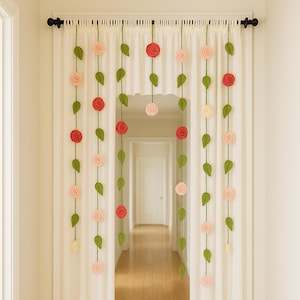 May include: A decorative curtain with a floral design. The curtain features rows of crocheted roses in shades of red and pink, interspersed with green leaves. The curtain hangs in front of a doorway, adding a touch of handmade charm to the space.