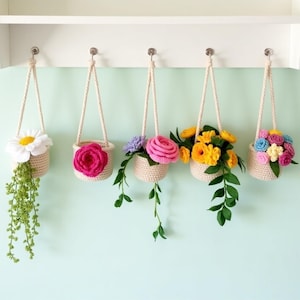 Może przedstawiać: Pięć wiszących donic z szydełka z kolorowymi kwiatami i zielenią. Każda donica to beżowy kosz z kremowym uchwytem z liny. Kwiaty obejmują białą stokrotkę, różową różę, fioletowe kwiaty, żółte kwiaty i mieszankę kolorowych kwiatów.
