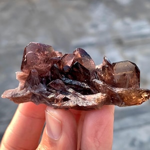 Puede incluir: Un racimo de puntas de cristal translúcidas de color púrpura oscuro y marrón con facetas angulares y afiladas. El espécimen mineral presenta una formación irregular y dentada con niveles variables de transparencia y tonos terrosos.