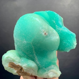 Puede incluir: Un vibrante esp&eacute;cimen mineral de color turquesa con una forma redondeada &uacute;nica. La superficie tiene una apariencia texturizada y cristalina. La base del mineral es de un color marr&oacute;n contrastante. La forma general es org&aacute;nica y llamativa.