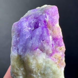 May include: A natural mineral specimen with a striking colour gradient. The top portion is a vibrant purple, transitioning to a lighter lavender hue, and then to a creamy, off-white base. The rough texture and crystalline structure are clearly visible.