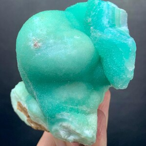 Puede incluir: Un vibrante esp&eacute;cimen mineral de color turquesa, con una forma redondeada y burbujeante. La superficie tiene un aspecto texturizado, con &aacute;reas de tonos turquesa m&aacute;s claros y oscuros. La base del mineral tiene un borde &aacute;spero y marr&oacute;n.