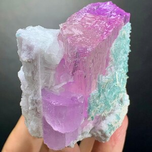 K&ouml;nnte beinhalten: Ein rohes Mineralexemplar mit durchscheinenden, leuchtend rosa und violetten Kristallstrukturen, die sich von einer texturierten, undurchsichtigen wei&szlig;en Matrix abheben. Die Gruppe zeigt zudem Bereiche mit hellt&uuml;rkisen Kristallformationen.