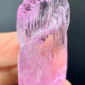 May include: A pink, translucent, faceted crystal with striations. The crystal is approximately 2 inches tall and has a slightly irregular shape.