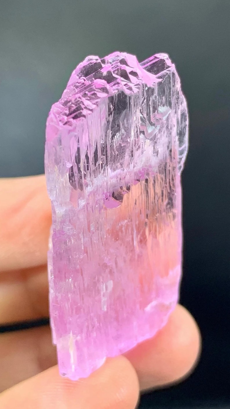 May include: A pink, translucent, faceted crystal with striations. The crystal is approximately 2 inches tall and has a slightly irregular shape.