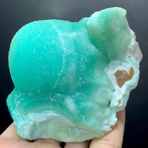Puede incluir: Un esp&eacute;cimen mineral de color turquesa vibrante con una textura redondeada y burbujeante. La piedra tiene &aacute;reas blancas y marrones, y una apariencia rugosa y natural. El mineral se sostiene en una mano, mostrando su tama&ntilde;o y variaciones de color.