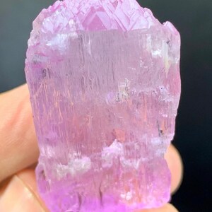 May include: A pink, translucent, faceted crystal with a striated surface. The crystal is approximately 2 inches tall and 1 inch wide.