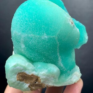 Puede incluir: Un vibrante esp&eacute;cimen mineral turquesa con una superficie texturizada y cristalina. El mineral tiene una forma redondeada y org&aacute;nica con una base m&aacute;s clara, blanquecina y un interior marr&oacute;n. La apariencia general es suave y llamativa.