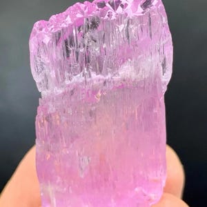May include: A pink, translucent, faceted crystal with a striated texture. The crystal is approximately 2 inches tall and has a rectangular shape.