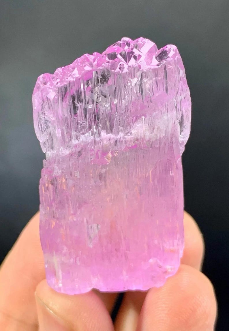 May include: A pink, translucent, faceted crystal with a striated texture. The crystal is approximately 2 inches tall and has a rectangular shape.