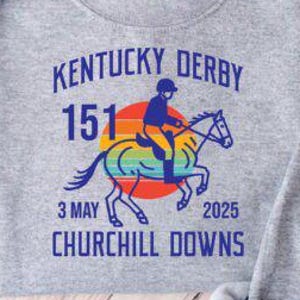 May include: Gray sweatshirt with a graphic design of a jockey riding a horse with a rainbow sunset behind them. The text reads "Kentucky Derby 151 3 May 2025 Churchill Downs".