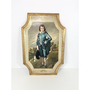 Puede incluir: Un retrato enmarcado de una persona joven con un traje azul, sosteniendo un sombrero. La pintura tiene un marco dorado con un fondo claro. La persona está de pie en una colina con árboles al fondo.