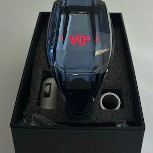 May include: A faceted, dark blue crystal car gear shift knob with the word "VIP" in red lettering. The knob is displayed in a black box with a silver-colored metal ring and a small, cylindrical piece.