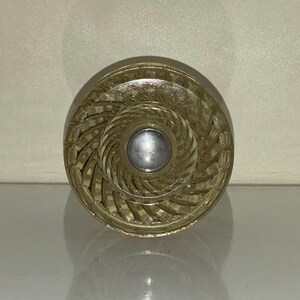 Peut inclure: Un bouton de porte en verre transparent avec un motif en spirale et un centre argenté. Le bouton a une surface texturée, probablement pour une armoire ou un tiroir.